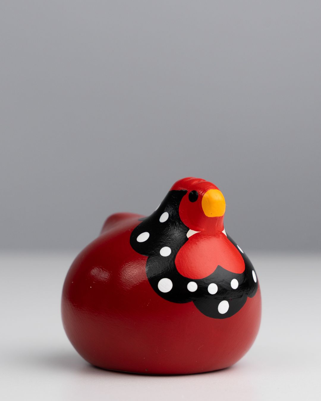 Red glazed ceramic hen with white polka dots on a grey studio backdrop