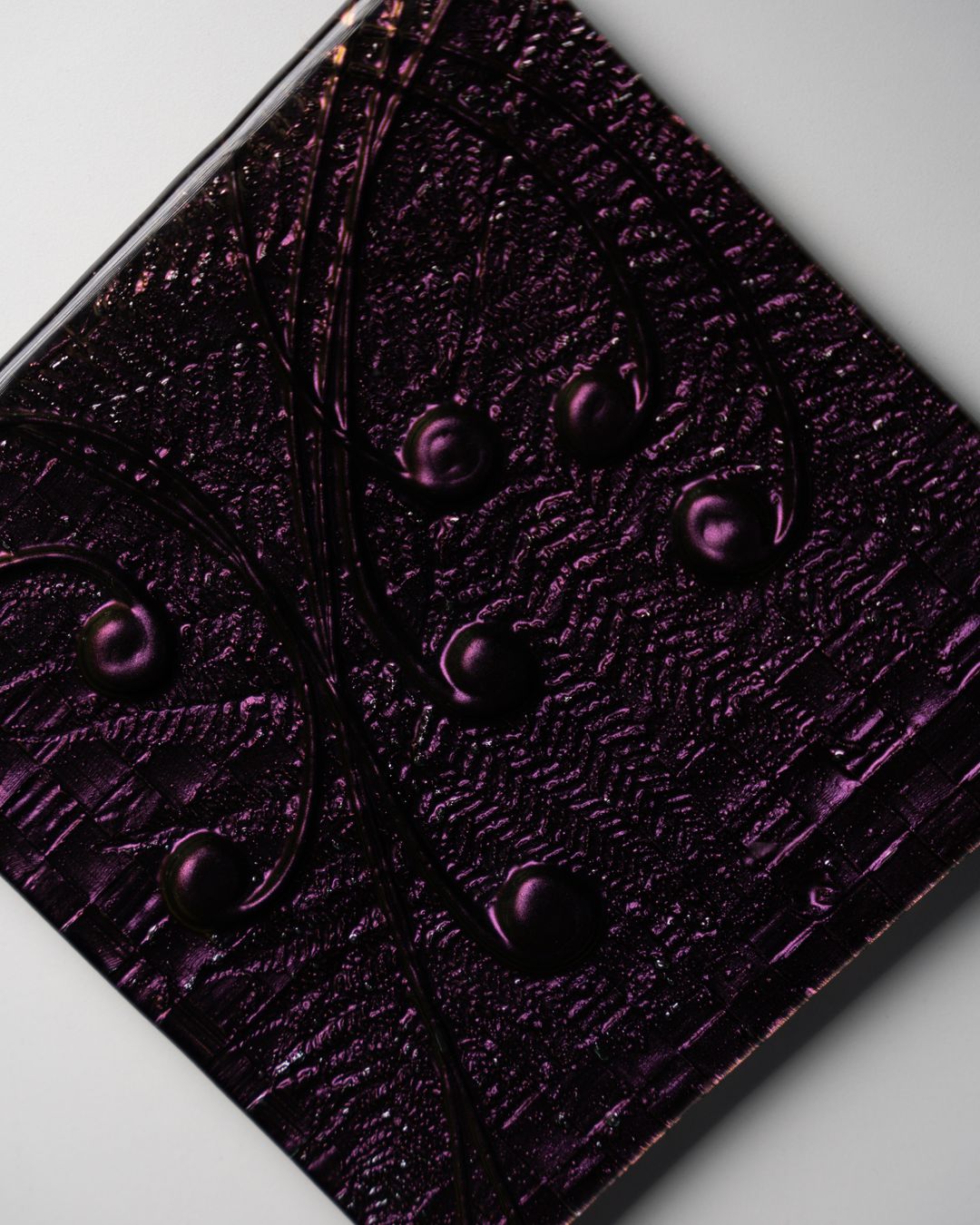 Close-up of a deep purple textured glass tile, lit to show its raised pattern